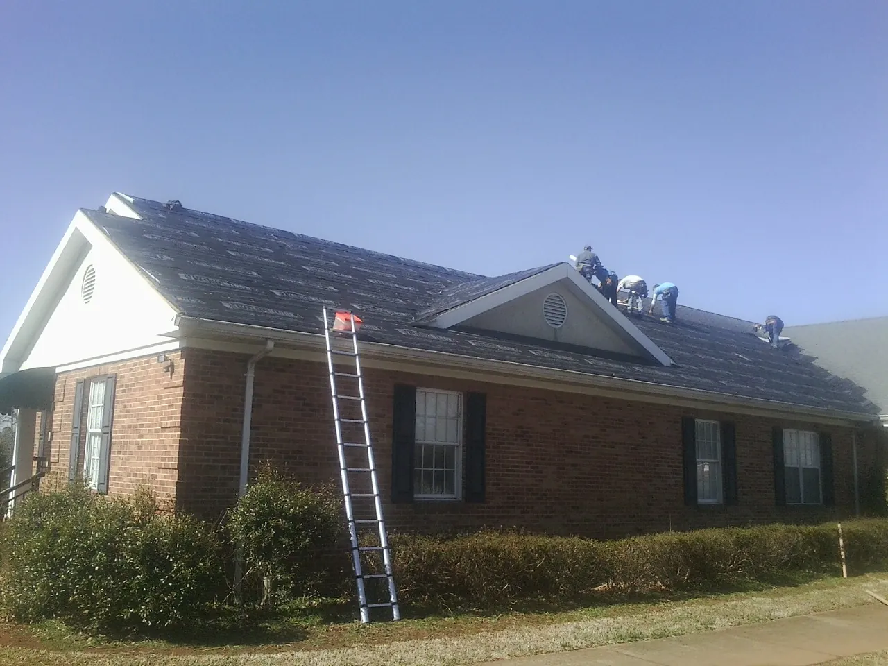Crew tearing shingles off a brick ranch roof with a ladder set — Metal Roof Repair work by our crew in Needham