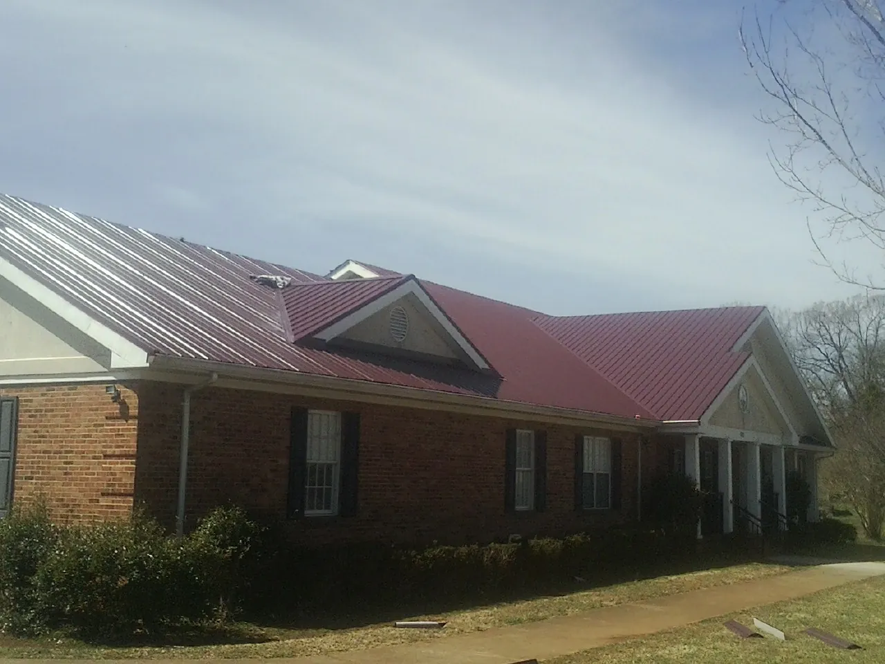 Red metal roof with gabled entries on a long brick building, from a Hail Damage Roof Repair job in Needham