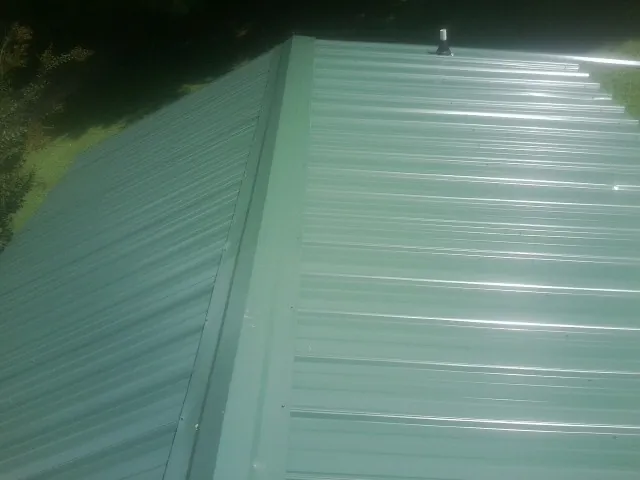 New green metal panels meeting at the ridge of a roof — Flat Roof Repair work by our crew in Needham