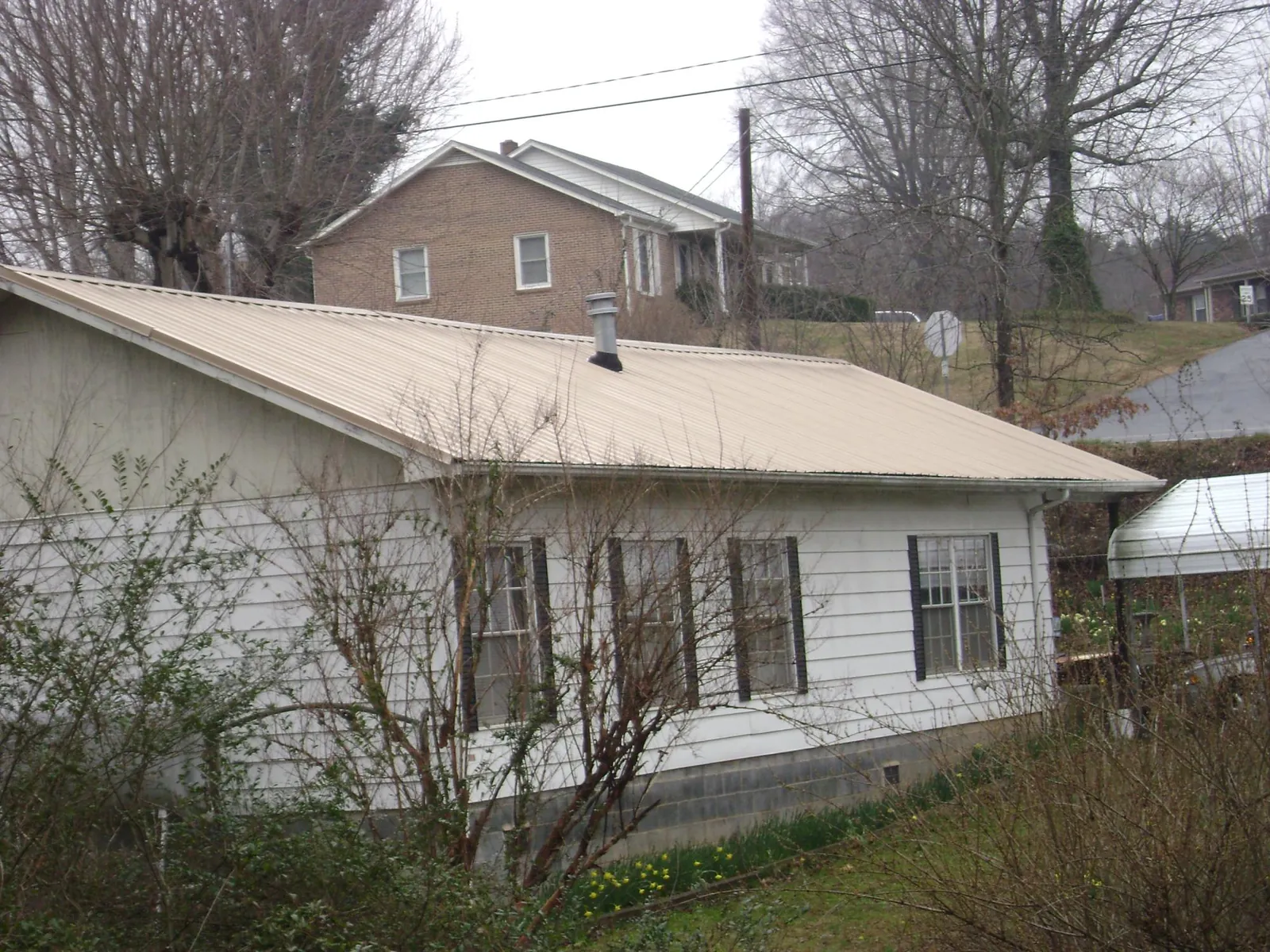 Tan metal roof on a white sided house set into a hillside — Commercial Roofing by Roofing Brothers in Needham